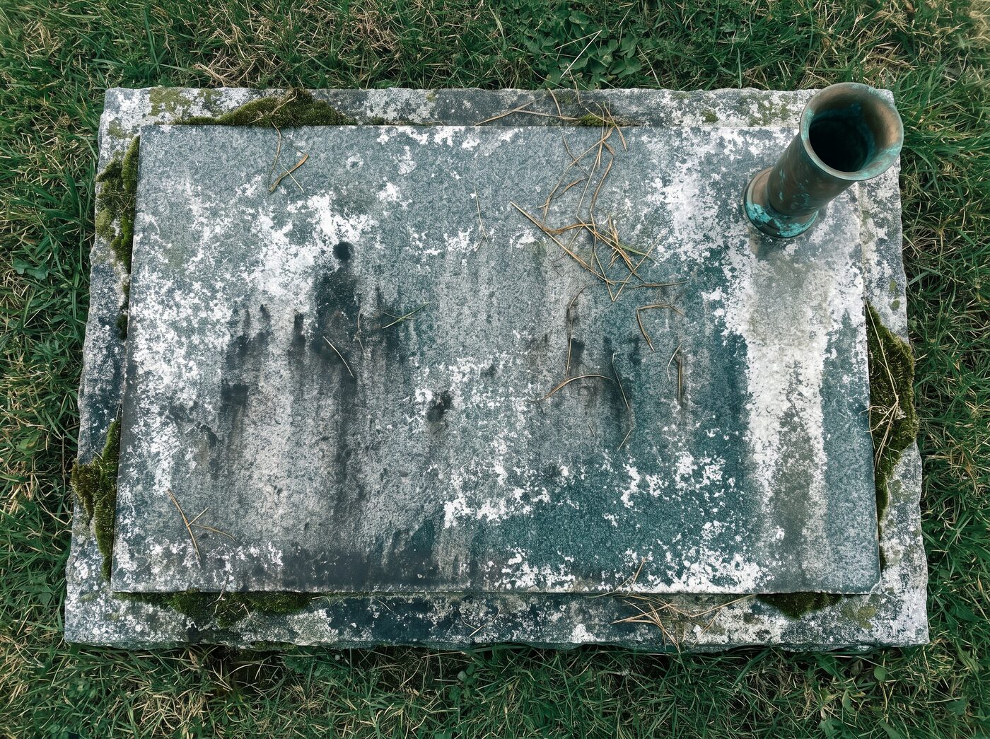 A flat granite marker covered in chalky mineral film and moss
